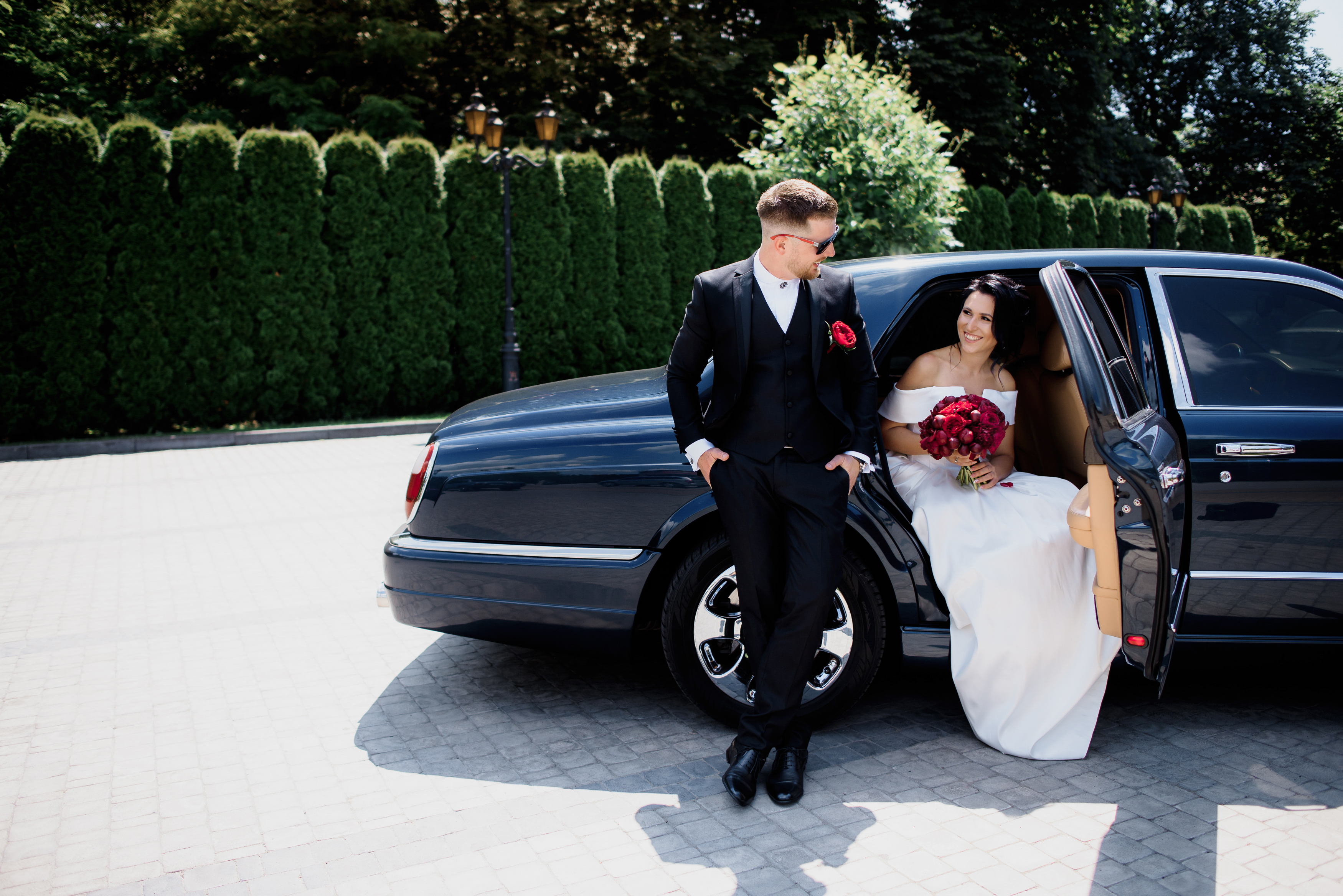 beautiful wedding couple is smiling in the black car on the sunn