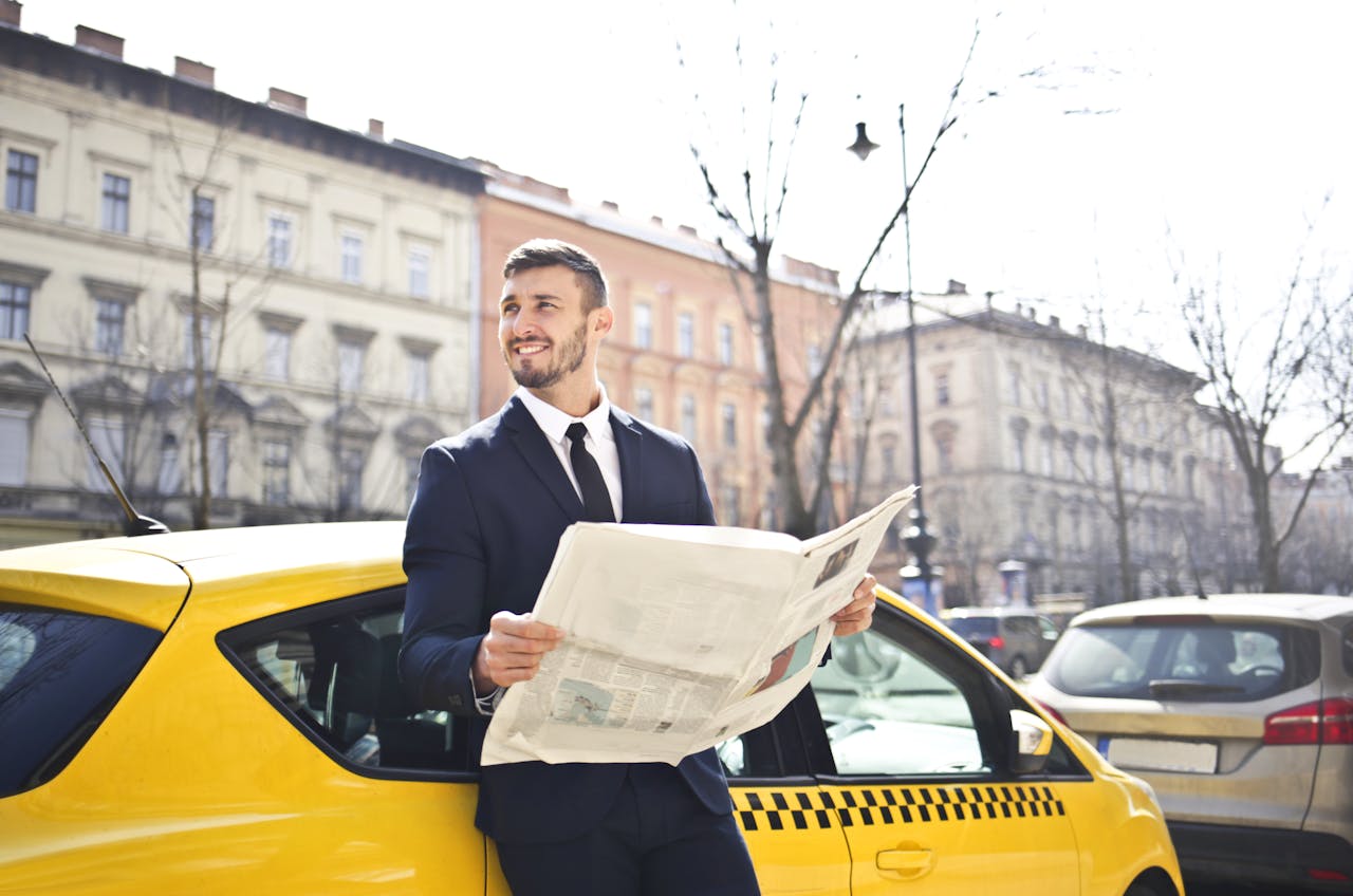 gallery-img-04 A businessman in a suit reads a newspaper while leaning on a yellow taxi in a city street.
